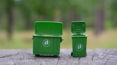 Plastik kahve fincanlarını ve küçük cam şişeleri ormandaki bir kütüğe yerleştirilmiş yeşil mini geri dönüşüm kutularına ayırmak için yakın plan..