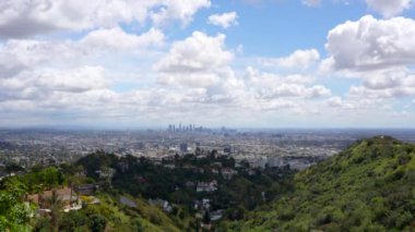 Los Angeles 'ın çarpıcı panoramik manzarası, yuvarlanan tepeler ve kalın, beyaz bulutlarla dolu bir gökyüzü, atmosferik ve resimsel bir manzara yaratıyor..