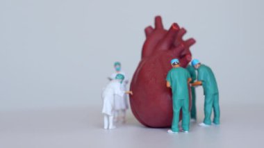 Minyatür cerrahların, sağlık ve tıp eğitimindeki takım çalışmalarını sembolize eden büyük bir kalp modelinde işbirliği yaptıkları dinamik bir sahne..