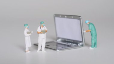 Minyatür doktor figürleri, uzun vadeli işlevsellik ve performansın sağlanması açısından planlanan bakımın önemini vurgulayan bir dizüstü bilgisayarı inceliyorlar..