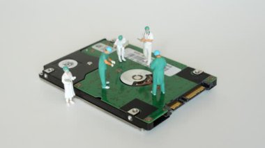 Sabit disk üzerinde çalışan cerrahların minyatür figürleri, veri kurtarma ve teknik onarımlardaki takım çalışmalarını sembolize ediyor.