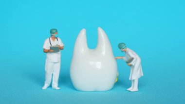 Üç minyatür diş hekimi dev bir diş modelini parlak mavi bir arka plana karşı inceliyor..
