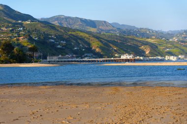 Malibu Rıhtımı 'nın sakin sulara uzanan manzarası, arka planda kumlu plaj ve tepeler, kıyı ve seyahat temaları için ideal..