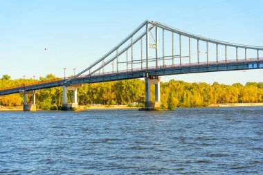 Kyiv 'de sonbahar renklerine ve temiz suya sahip Dinyeper Nehri boyunca uzanan Parkovyy Köprüsü' nün yan görüntüsü.
