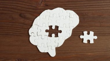 Ahşap bir yüzeydeki diğer parçalar tarafından oluşturulan ve bilişsel süreçleri sembolize eden bir yapboz parçasının içine yerleştirilen elin yakın çekimi..