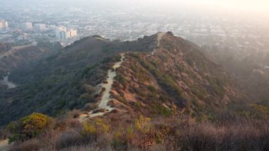 Altın Saat Manzarası Runyon Canyon Parkı 'ndaki viraj ve tepeleri gösteriyor. Arka planda Los Angeles gökdelenleri var..