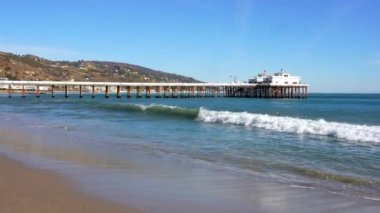 Malibu, California - 29 Kasım 2024: Malibu Rıhtımı 'nın açık mavi gökyüzünün altında sörf yapan bir sörfçü ve bir kanocunun kürek çekişini gösteren manzarası.