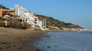 Malibu, California - 29 Kasım 2024: Malibu sahilinin büyüleyici manzarası Kafelerden hoşlanan ve kumlu sahil boyunca yürüyen insanlar.