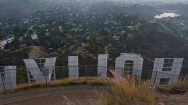 Los Angeles, Kaliforniya - 9 Aralık 2024 Hollywood tabelasının arkasından büyüleyici manzara, büyüleyici altın saat boyunca puslu tepeler, şehir manzarası ve gölü gözler önüne seriyor..