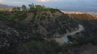 Runyon Canyon 'daki dolambaçlı yolları ve arka planda geniş Los Angeles şehrini içeren çarpıcı bir akşam manzarası..