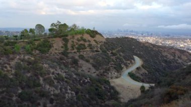 Runyon Canyon 'daki yamaçlar arasındaki sarmal yolun sakin manzarası bulutlu bir günde Los Angeles ufuk çizgisini gösteriyor..