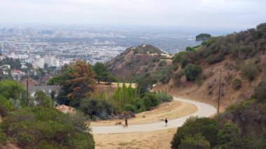 Los Angeles, Kaliforniya - 13 Aralık 2024 Runyon Canyon 'da bulutlu bir günde Los Angeles manzaralı dolambaçlı bir yolda yürüyen ziyaretçiler.