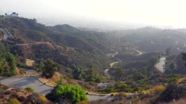 Hollywood Dağı 'nın güney yamacından Griffith Park' ı, Gözlemevi 'ni, virajlı yolları ve Los Angeles' ın sisli ufuk çizgisini görüyoruz..