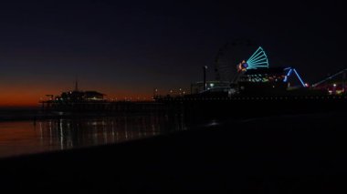 Los Angeles, California - 18 Aralık 2024: Santa Monica İskelesi 'nin gece manzarası, alacakaranlıkta sakin okyanus sularına yansıyan dönme dolap da dahil olmak üzere renkli ışıklarla.