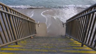 Kumlu kumsala inen merdivenler ve yumuşak dalgalar Malibu, California 'daki huzurlu okyanus kıyısına ulaşma imkanı sunuyor..
