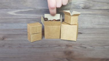 Kavrulmuş kahve çekirdekleri ile dolu iki minyatür kutuyu çevirip, onları ahşap bir yüzeye döküyor, kahve paketleme ve işleme önem veriyor..
