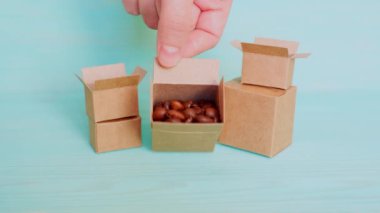 Minyatür karton kutular içinde kavrulmuş kahve çekirdekleri var. Hepsini tek tek çıkarıyorlar. Açık mavi bir arkaplanda diziliyorlar..