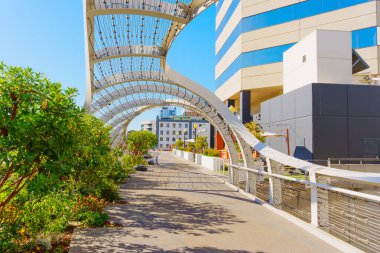 Long Beach, California - January 15, 2025: Curved architectural walkway with vibrant greenery alongside modern buildings at Long Beach Convention and Entertainment Center. clipart