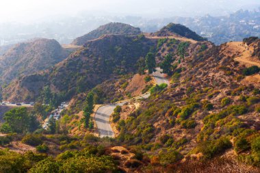 Griffith Park 'ın tepelerinde dolambaçlı yollar, yemyeşil ve uzak şehir hatlarının manzaralı manzarasını sergiliyor.