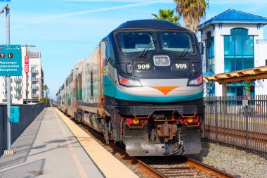 Oceanside, California - 26 Aralık 2024: Oceanside, Kaliforniya 'daki Metrolink 909 tren motorunun yakın görüntüsü. İstasyon platformunda parlak güneş ışığı altında tren rayları ve otelin arka planı yer alıyor.