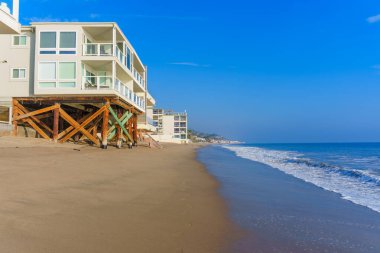 Malibu, California - 21 Aralık 2024: canlı sahil evleri ve dingin okyanus dalgalarıyla Malibu plajı güzelliği. Sahil yaşam tarzı ve tatil temaları için mükemmel bir zemin.