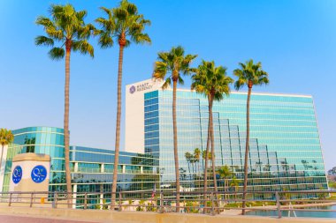 Long Beach, California - 11 Ocak 2025: Long Beach, Kaliforniya 'daki Hyatt Regency Oteli, palmiye ağaçları ve açık mavi gökyüzü ile çevrili, geniş açılı bir görüntüye sahiptir..