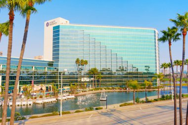 Long Beach, California - 11 Ocak 2025: Long Beach, Kaliforniya 'daki Modern Hyatt Regency Hotel' de cam mimarisi, palmiye ağaçları ve geniş açılı perspektifli bir rıhtım manzarası yer almaktadır..