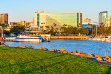 Long Beach, California - 11 Ocak 2025: Modern Hyatt Regency Oteli, Long Beach limanı yakınlarında, parlak günbatımı batımında palmiye ağaçları ve botlarla cam mimari sergilenmektedir..