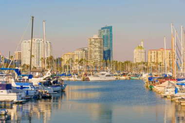 Long Beach, California - 11 Ocak 2025: Gökkuşağı Limanı 'nın limanlarını gösteren manzara, çeşitli tekneler, berrak sular ve günbatımında yükselen gökdelen binaların arka planı.