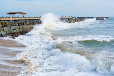 Dinamik okyanus dalgaları Cabrillo Sahili İskelesi 'ndeki kayalık iskeleye çarpar. İskele manzarası, kumlu sahil manzarası ve parlak bir gökyüzü altında ufuk çizgisi..