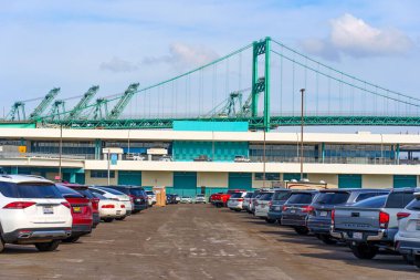 Los Angeles, Kaliforniya - 25 Aralık 2024: Arkaplanda Los Angeles Limanı 'nın altyapı ve gantry vinçlerini açık bir gökyüzünün altında gösteren çeşitli arabalarla dolu hareketli bir otopark.