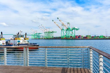 Los Angeles, Kaliforniya - 25 Aralık 2024: Rıhtımlı Delta Audrey römorkörü, dev yeşil kanat vinçleri ve ön planda ahşap bir korkuluk ile Los Angeles Limanı manzarası.