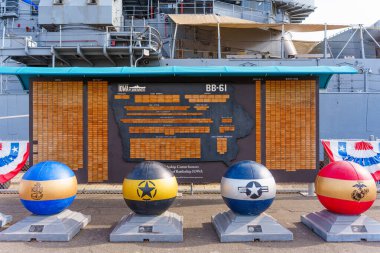 Los Angeles, Kaliforniya - 25 Aralık 2024: USS Iowa plankowners anısına bir tahta duvar, donanma amblemi ve savaş gemisi arkaplanına karşı renkli hatıra küreleri.