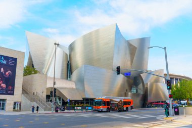 Los Angeles, Kaliforniya - 4 Aralık 2024: Walt Disney Konser Salonu 'nun önünden geçen bir otobüs ve Los Angeles' ta yaya geçidinde trafik işaretini bekleyen yayalar.