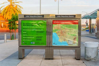Los Angeles, Kaliforniya - 4 Aralık 2024: Küçük Tokyo 'da bir metro istasyonunda canlı bir tabela, haritalar ve toplu taşıma bilgileri, palmiye ağaçları ve sıcak bir akşam parıltısı üzerine kurulmuş.