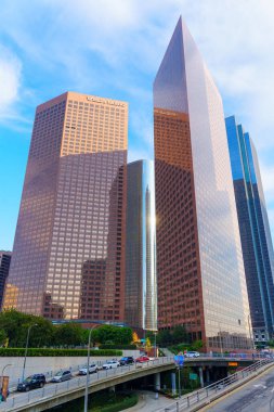 Los Angeles, Kaliforniya - 4 Aralık 2024: Otoyol üst geçidi ve ön planda park edilmiş arabaları olan Massive Wells Fargo Center gökdeleni, Los Angeles şehir merkezinde açık mavi bir gökyüzüne karşı kurulmuştur.