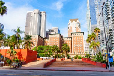 Los Angeles, California - 3 Aralık 2024: Los Angeles şehir merkezinde açık mavi gökyüzü altında palmiye ağaçları ve modern mimarinin yer aldığı canlı Pershing Meydanı manzarası.
