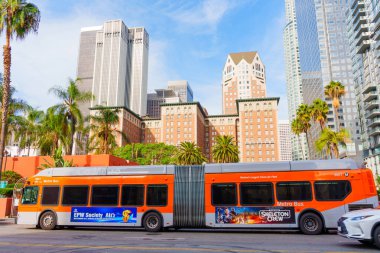 Los Angeles, Kaliforniya - 3 Aralık 2024: Los Angeles Metro otobüsü Pershing Meydanı 'ndan geçiyor, öğleden sonra açık bir gökyüzü altında modern mimari ve palmiye ağaçları sergileniyor..