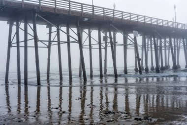 Sisli bir sabahta Oceanside Belediye İskelesi 'nin geniş açılı görüntüsü iskelenin yapısını ve ıslak kumdaki yansımalarını gözler önüne seriyor..