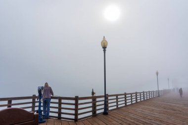 Oceanside, California - 3 Ocak 2025: Balıkçı Kaliforniya 'daki Oceanside Belediye İskelesi' nde duruyor, sisle çevrili, deniz kenarında sakin bir anı yakalıyor..