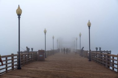 Oceanside, California - 3 Ocak 2025: Oceanside Belediye İskelesinde sakin sisli bir sabah balıkçıların ve ahşap güvertede gezginlerin olduğu, yumuşak ortam aydınlatmasıyla vurgulanan.