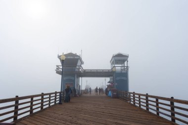 Oceanside, California - 3 Ocak 2025 Oceanside Belediye İskelesi 'nde sisli bir sabah, tahtadan bir kaldırım, cankurtaran kulesi ve bir yem dükkanı, sakin bir sahil atmosferi sergiliyor..