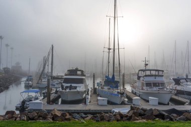 Oceanside, California - 3 Ocak 2025: Okyanus kıyısında sakin bir marina, günbatımında sisle örtülü botlarla yakalanarak, sakin ve atmosferik bir ortam yaratıldı..