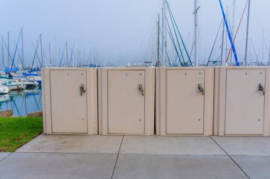 Oceanside, California - 3 Ocak 2025: Bej depolama dolapları Oceanside Limanı, Kaliforniya 'da duruyor, yelkenliler sisli arka planda demirlemiş, sabah ışığı altında yakalanmış..