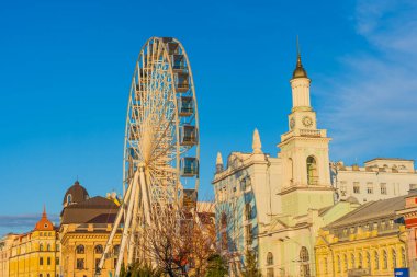 Kyiv, Ukrayna - 28 Mart 2025: Kyiv 'deki Kontraktova Meydanı' nın canlı görüntüsü, açık mavi gökyüzüne karşı geniş bir dönme dolap sergiliyor, tarihi mimariyi ve kentsel atmosferi vurguluyor.