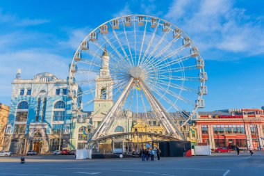 Kyiv, Ukrayna - 28 Mart 2025: Kyiv, Ukrayna 'daki Kontraktova Meydanı' nda parlak binalar ve açık mavi gökyüzü ile büyük dönme dolap.