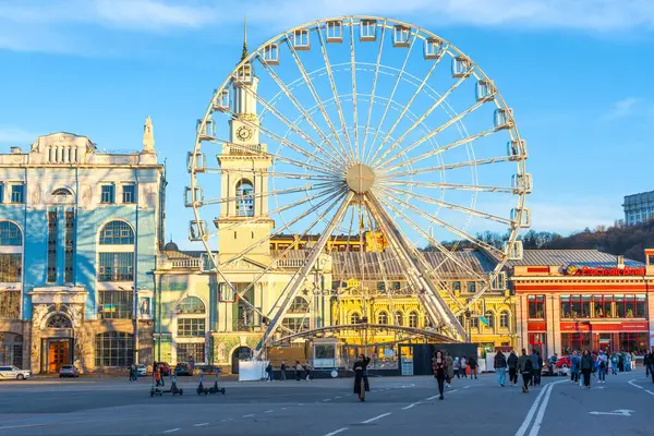 Kyiv, Ukrayna - 28 Mart 2025: Kyiv 'deki Kontraktova Meydanı' nın geniş açılı görüntüsü, açık mavi gökyüzüne karşı ikonik dönme dolabı gösteriyor, insanlar ön planda geziniyor..
