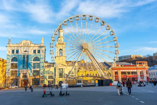 Kyiv, Ukrayna - 28 Mart 2025: Kyiv, Ukrayna 'daki Kontraktova Meydanı' nın geniş açılı görüntüsü, altın saat boyunca açık mavi bir gökyüzü altında büyük bir dönme dolap ve tarihi binalar sergiliyor..