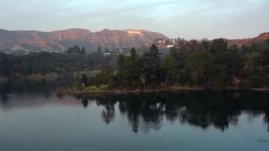 Los Angeles, California - 5 Ocak 2025: Hollywood Gölü 'nün panoramik manzarası tepelerdeki ikonik Hollywood tabelasını vurguluyor, günbatımı gökyüzünü ve sakin su yansımalarını gösteriyor.
