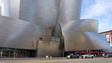 Los Angeles, Kaliforniya - 7 Ocak 2025: Genç adam, Walt Disney Konser Salonu 'nun yakınlarındaki kaldırımda bir müzik videosu kaydederken enerjik bir şekilde jest yapıyor.